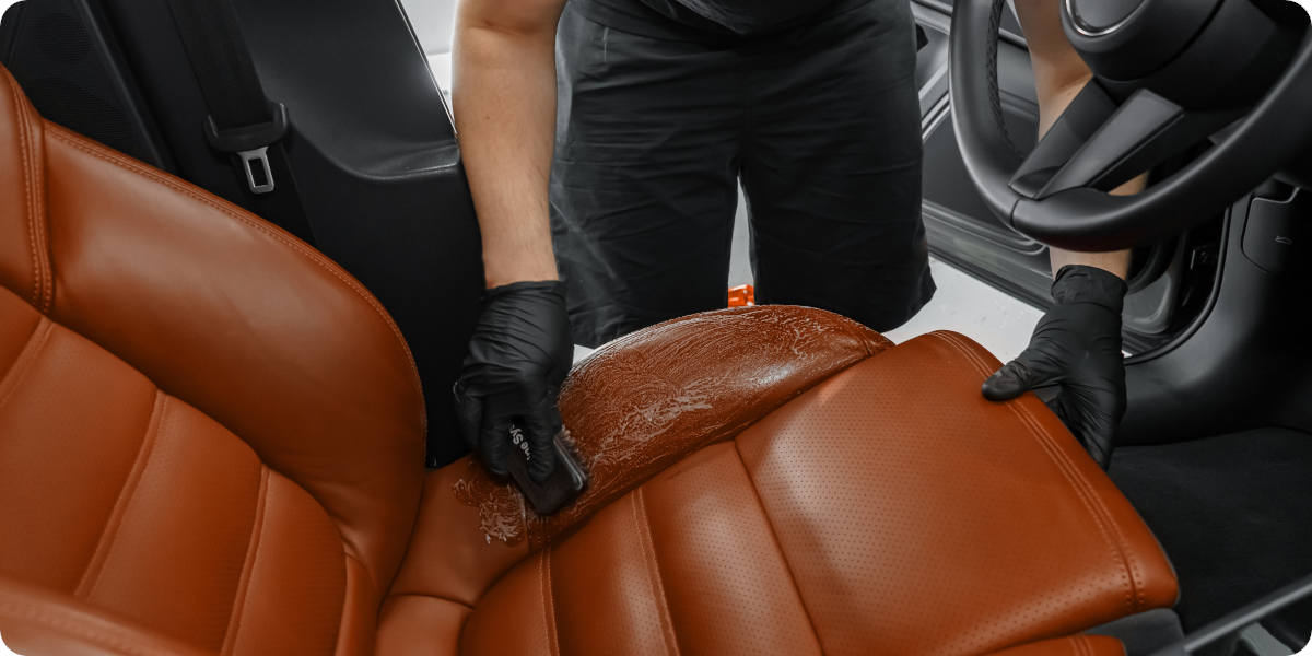 Brauner Ledersitz im Auto wird mit Pflegemittel und Schwamm sorgfältig gereinigt.
