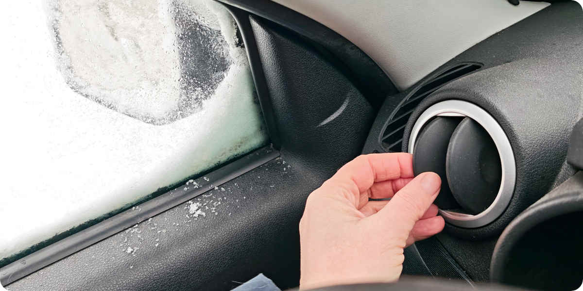 Eine Hand richtet die Lüftung im Auto auf die gefrorene Scheibe der Fahrertür.