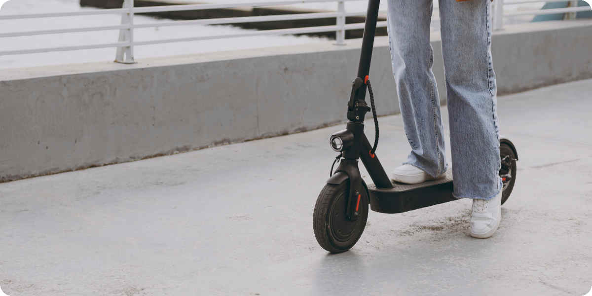Eine Person steht mit einem Bein auf einem schwarzen E-Scooter.