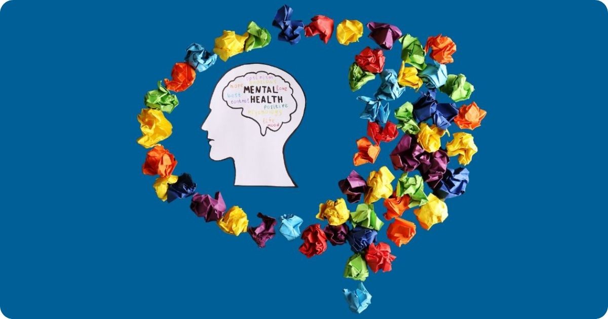 Eine aus weißem Papier ausgeschnittene Kopfsilhouette mit den Worten "mental health" beschriftet umrandet von vielen bunten Papierknöllchen.