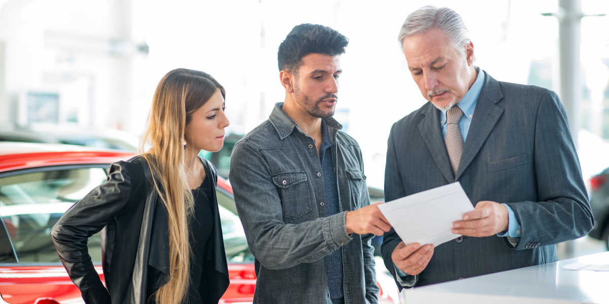 Ein Autohändler berät ein Paar bezüglich einer Autofinanzierung.