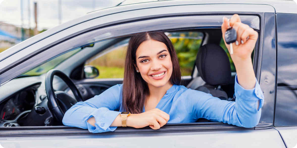 Eine Frau sitzt im Auto und zeigt die Autoschlüssel durch das Fenster.