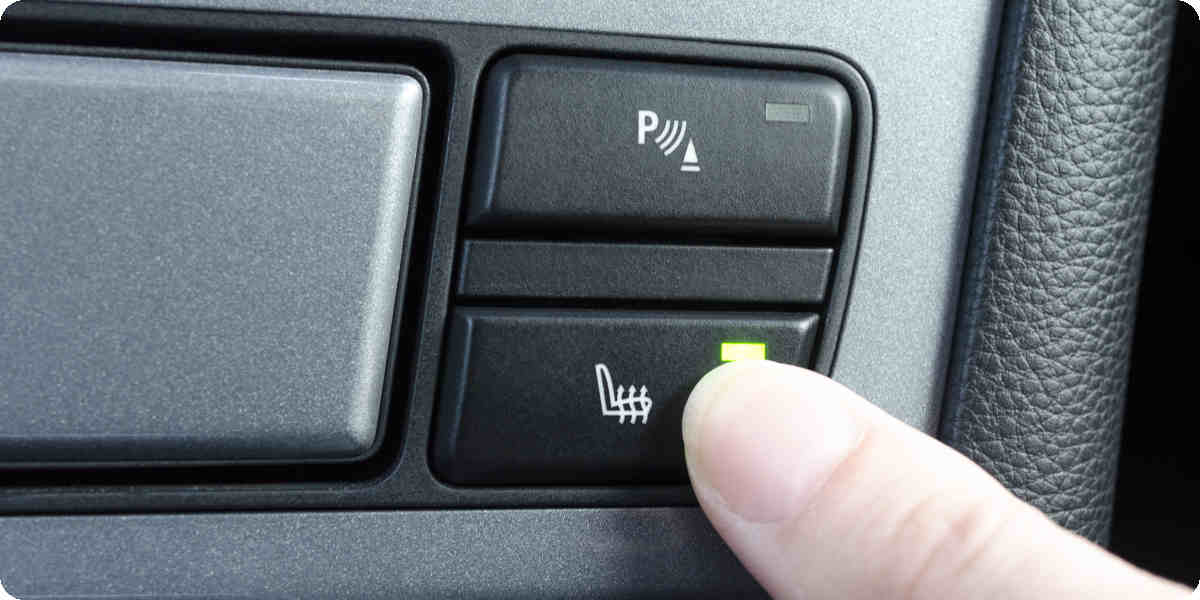 Person zeigt auf den Knopf für die Sitzheizung im Auto.