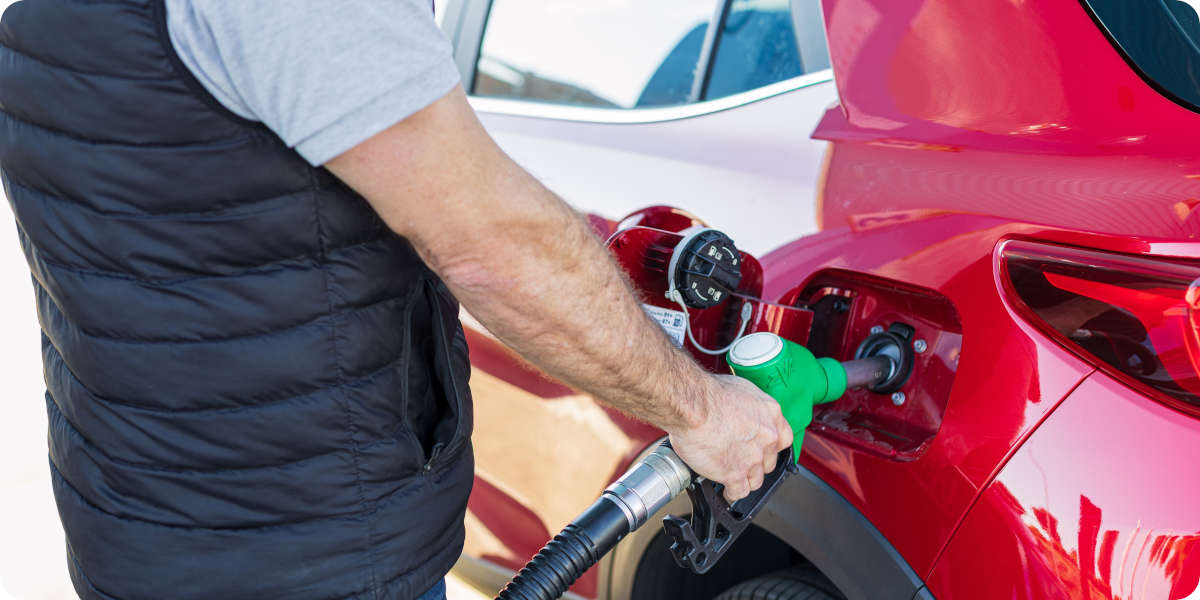Person tankt ein rotes Auto mit einer grünen Zapfpistole an der Tankstelle.
