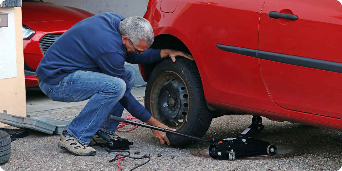 Ein Mann wechselt benutzt einen Wagenheber um ein Auto anzuheben und den Reifen zu wechseln.