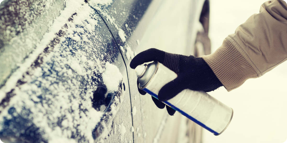 Eine Person sprüht ein Enteisungsspray auf eine zugefrorene Autotür.