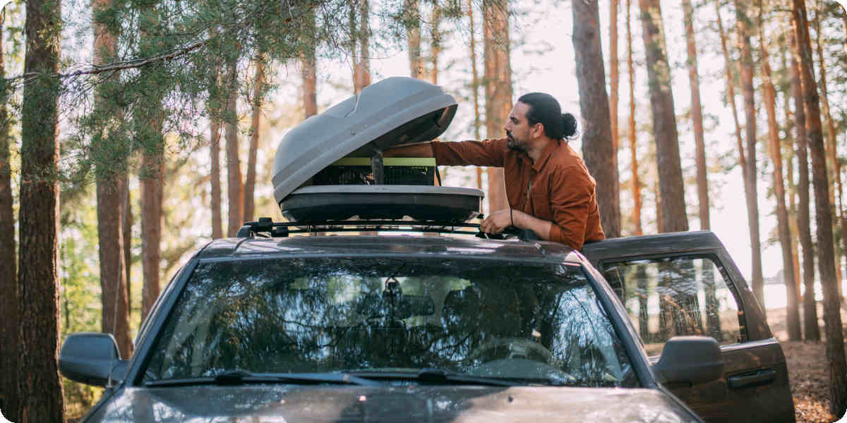 Ein Mann befüllt in der Natur seinen Dachgepäckträger auf dem Auto.