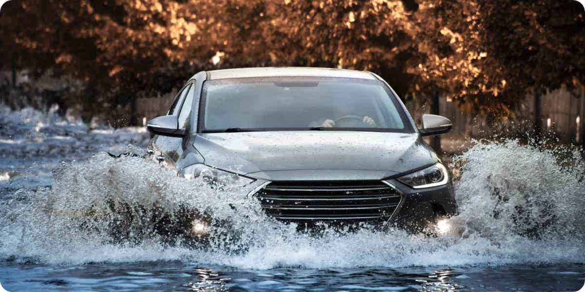 Ein graues Auto fährt mit hoher Geschwindigkeit durch Hochwasser.