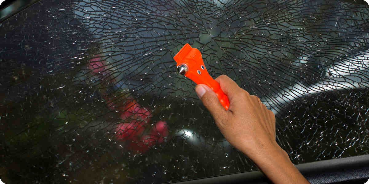 Eine Frau schlägt mit einem Sicherheitshammer eine Scheibe im Auto ein.