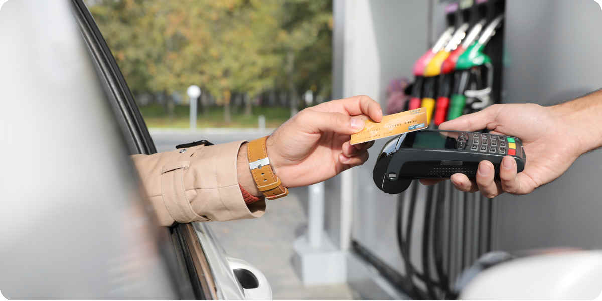 Eine Person hält eine Kreditkarte aus dem Autofenster und bezahlt damit sein Benzin.