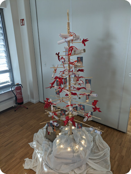 Fotografie von einem selbst gebauten Weihnachtsbaum mit gerollten Zetteln und roten Schleifen an den Zweigen.
