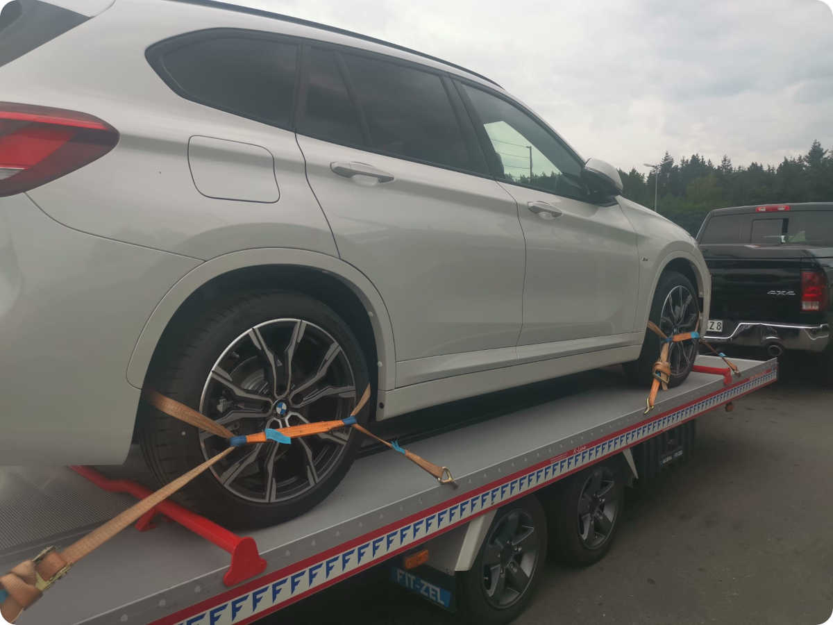 Ein weißes Auto wurde auf einer Ladefläche eines Anhängers für die Überführung auf Fremdachse befestigt.
