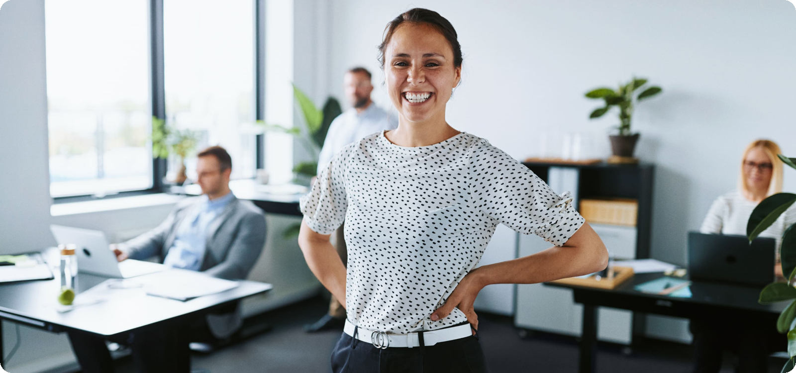 Eine Frau steht im Büro und lächelt in die Kamera.