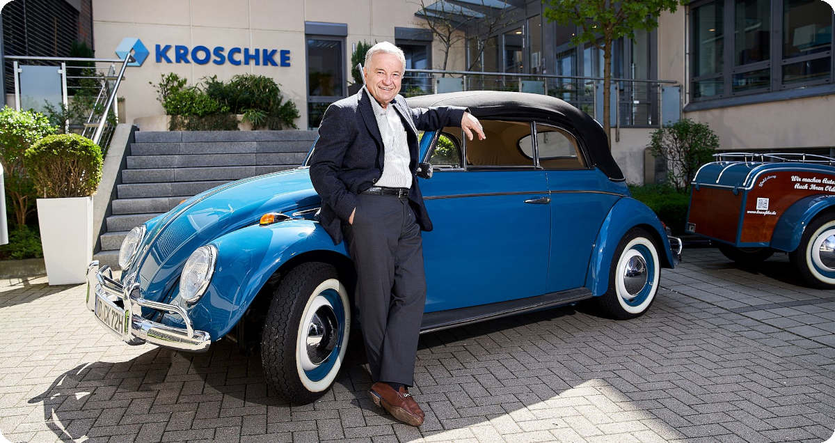 Christoph Kroschke lehnt sich an einen blauen VW Käfer und lächelt in die Kamera.